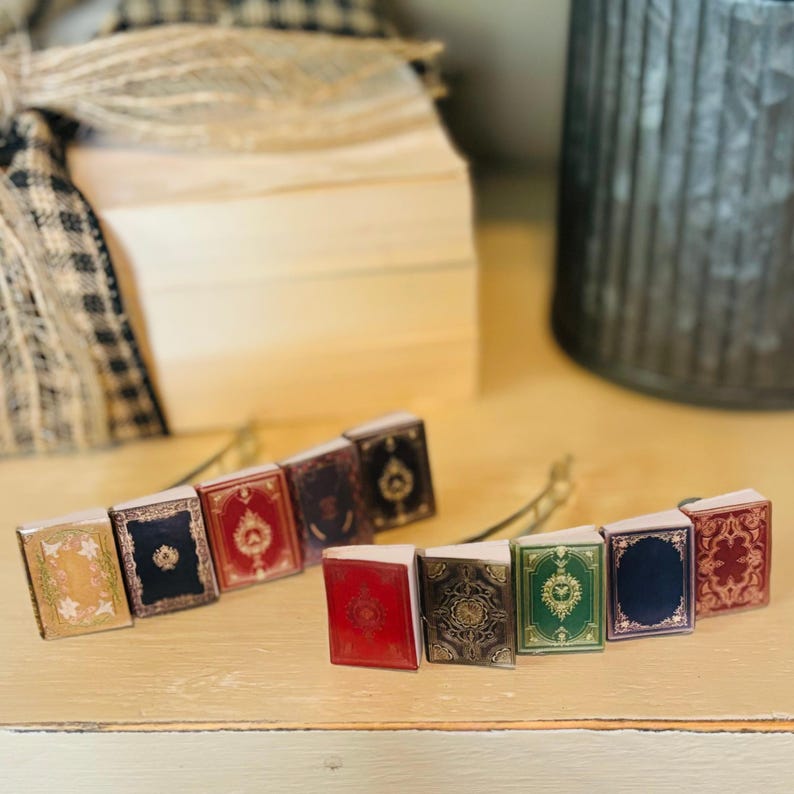May include: Two sets of miniature book-shaped hair clips. One set has five clips in shades of red, green, blue, and gold. The other set has four clips in shades of red, gold, and blue.