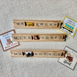 Handmade Scrabble tile name plate with custom names and decorative charms including apple, bus, bee, sports balls, and more. A fun, unique teacher desk accessory or coach gift, ideal for back-to-school or end-of-year presents.