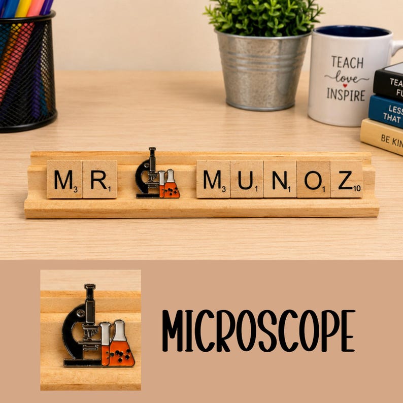 Op de afbeelding: Een houten tegelhouder met de naam MR. MUNOZ, met een metalen emaille speld van een zwarte microscoop en oranje met vloeistof gevulde bekers tussen de letters geplaatst. De tegels zijn voorzien van zwarte letters op een lichte houten achtergrond.