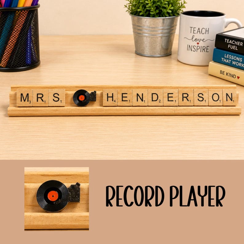 Op de afbeelding: Een lichtgekleurde houten standaard met de naam MRS. HENDERSON in vierkante lettertegels. Een klein zwart en oranje icoon van een platenspeler staat tussen de woorden. De tegels bevatten zwarte letters en kleine numerieke waarden.