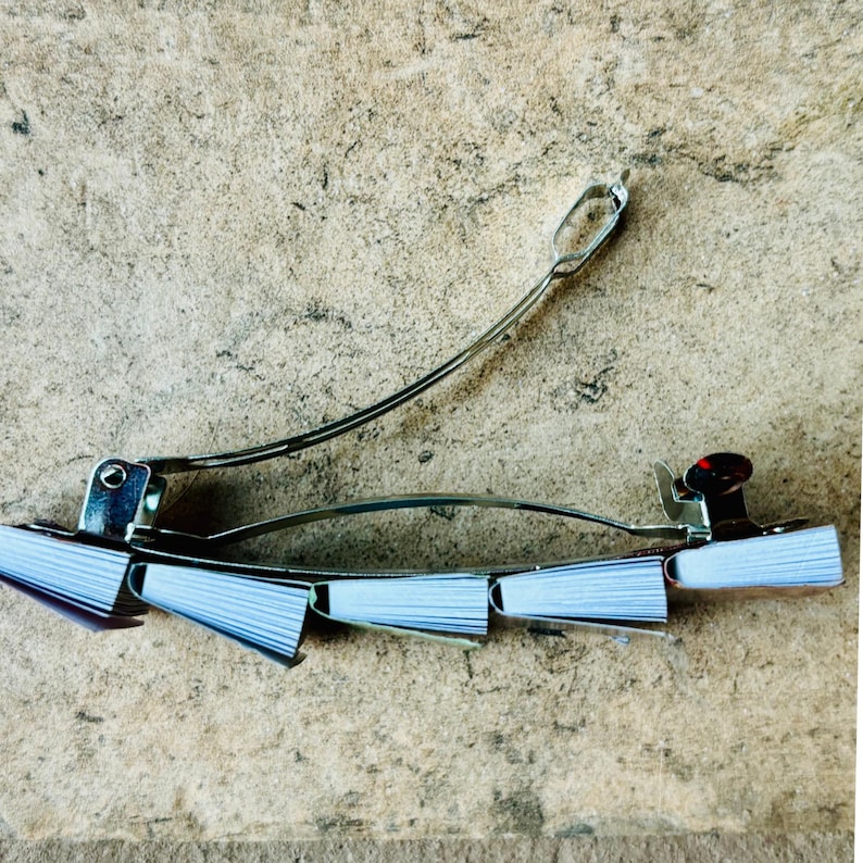 May include: A silver hair clip with a decorative design of small, white, paper-like fans. The clip is open and ready to be used.
