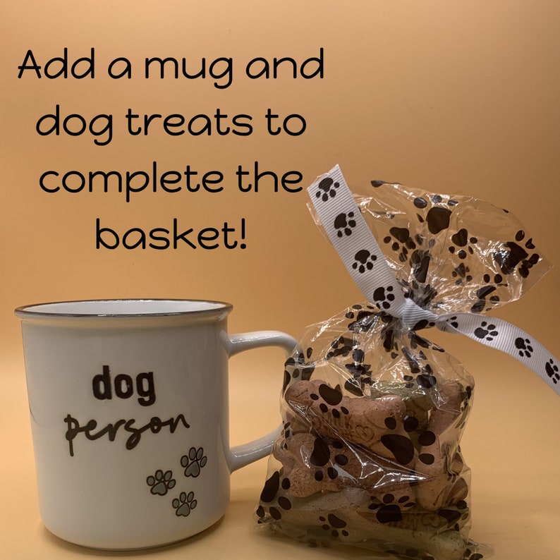 May include: White ceramic mug with black text that reads "dog person" and gray paw prints. A clear plastic bag filled with dog treats tied with a white ribbon with black paw prints.