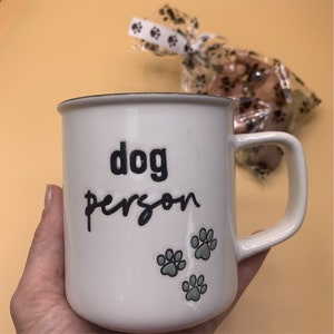 May include: White ceramic mug with black text that reads "dog person" and three green paw prints.