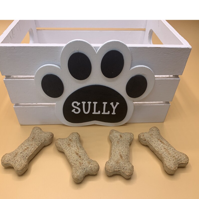 May include: White wooden crate with a black paw print and the name "SULLY" on it. Four dog biscuits are in front of the crate.
