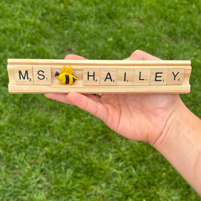 Custom Scrabble tile desk name plate with wooden base and fun themed embellishments. Perfect for teachers, coaches, and staff gifts. Makes a thoughtful classroom desk decoration or personalized gift for back-to-school and appreciation