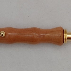May include: A wooden thread cutter with a gold-colored handle and a red tip. The cutter has a small metal loop at the end of the handle.
