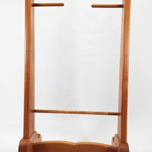 May include: A wooden stand with two horizontal bars for displaying items. The stand has a decorative top and bottom edge and is made of light brown wood.
