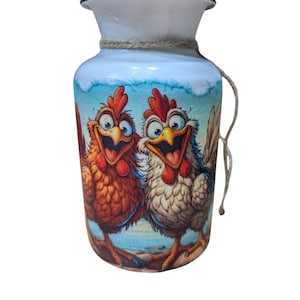 May include: White ceramic vase with a cartoon illustration of two chickens. The chickens have red combs and are smiling. The vase has a rope detail around the neck and a white rim.