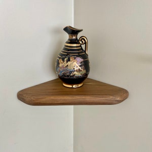 May include: A dark brown wooden corner shelf with a black and gold ceramic pitcher with a painted scene of figures.