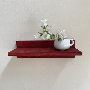 May include: A red wooden shelf with a white ceramic pitcher filled with white bell-shaped flowers.