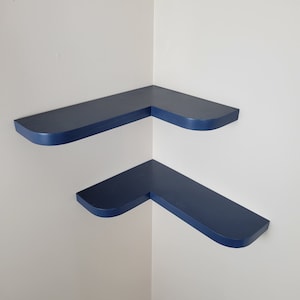 May include: Two blue corner shelves with rounded edges. The shelves are mounted on a white wall.