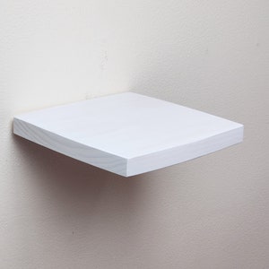 May include: A white wooden shelf with a slightly curved edge. The shelf is mounted to a white wall.