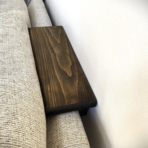 Op de afbeelding: Een donkerbruin houten plank bevestigd aan de zijkant van een bank. De plank is gemaakt van hout met een natuurlijke houtnerf.