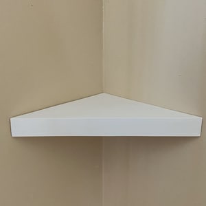 Könnte beinhalten: Ein weißes Eckregal aus Holz. Das Regal ist dreieckig und an einer Wand montiert.