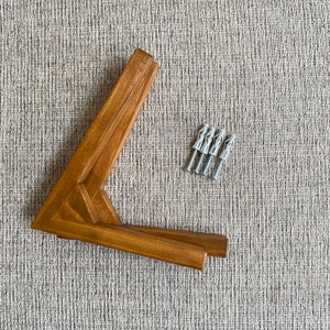 May include: A set of four brown wooden corner brackets with four silver wall anchors.