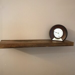May include: A brown wooden shelf with a clock on it. The clock has a brown face with white numbers and hands.