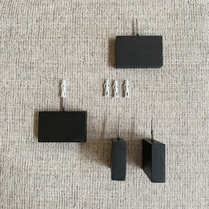 May include: A collection of black wooden furniture legs and small white decorative figurines. The legs are rectangular and square, with metal screws. The figurines are small, white, and appear to be statues.