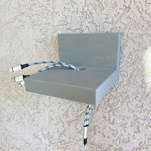 May include: A gray wooden wall mount with a hole for cords. Three white and black cords are threaded through the hole.