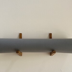 May include: A gray yoga mat is hanging on a wall mounted wooden rack. The rack is made of two pieces of wood that are connected at a right angle.