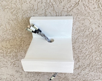 Puede incluir: Estante de pared de madera blanca con un agujero para cables. Tres cables negros y blancos se enhebran a través del agujero y salen por la parte inferior del estante.