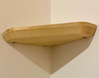 May include: A natural wood corner shelf with a rounded edge and a light wood finish. The shelf is mounted to a wall with screws.