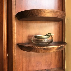 May include: A glass ashtray with a brass insert and a small brass handle sits on a wooden shelf. The shelf is part of a wooden cabinet with a dark wood finish.