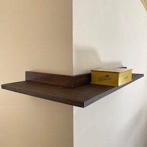 May include: A dark brown wooden shelf mounted on a white wall with a yellow box labeled "Whitman's" on top.