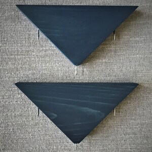 May include: Two dark blue triangular shelves mounted on a textured wall. The shelves are made of wood and have a simple, modern design.