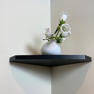 May include: A black corner shelf with a white ceramic vase holding white bell-shaped flowers.