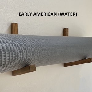 May include: A gray yoga mat is hanging on a wall using two wooden wall mounts. The text "EARLY AMERICAN (WATER)" is printed on the wall above the mat.
