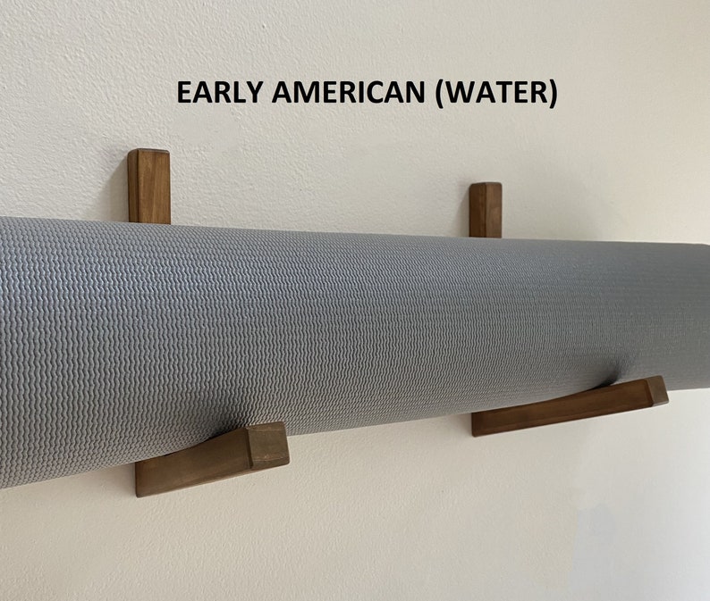 May include: A gray yoga mat is hanging on a wall using two wooden wall mounts. The text "EARLY AMERICAN (WATER)" is printed on the wall above the mat.