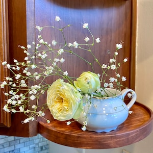 May include: A white porcelain creamer with a gold trim, filled with a bouquet of white baby's breath and two yellow roses.