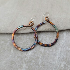 Może przedstawiać: Para iryzujących miedzianych kolczyków koła z młotkowanym wykończeniem i srebrnymi haczykami.