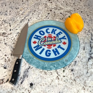 Puede incluir: Una tabla de cortar redonda de vidrio azul y blanco con el texto "Hockey Night in Canada" en un círculo rojo, blanco y azul. Un pimiento amarillo está sobre la tabla de cortar.