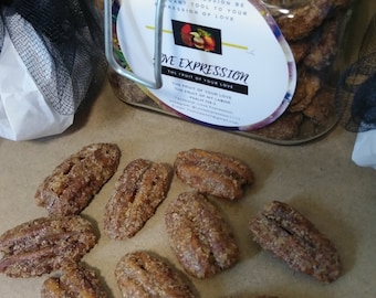 May include: A glass jar filled with pecan halves coated in a brown sugar glaze. The jar has a metal clasp and a label that reads "Love Expression: The Fruit of Your Love". There are also several pecan halves scattered on a brown surface.