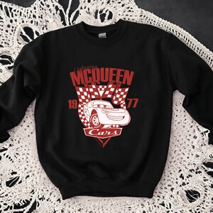 Puede incluir: Sudadera negra con un gr&aacute;fico rojo de Rayo McQueen de la pel&iacute;cula Cars. El gr&aacute;fico incluye el texto "Lightning McQueen" y "Cars" con un dise&ntilde;o de bandera a cuadros.