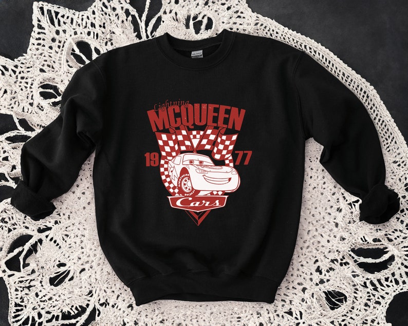 Puede incluir: Sudadera negra con un gr&aacute;fico rojo de Rayo McQueen de la pel&iacute;cula Cars. El gr&aacute;fico incluye el texto "Lightning McQueen" y "Cars" con un dise&ntilde;o de bandera a cuadros.