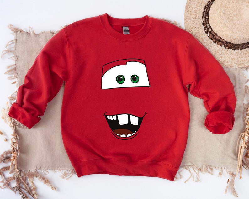 May include: Red sweatshirt with a cartoon face of a red car with green eyes and a toothy grin.