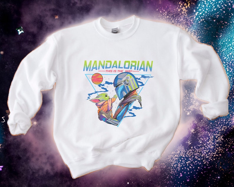 May include: White sweatshirt featuring a graphic print of a Mandalorian character holding a small green alien. The text "MANDALORIAN -THIS IS THE WAY- " is printed above the graphic.