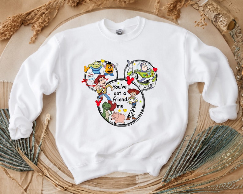 Puede incluir: Sudadera blanca con un gr&aacute;fico de personajes de la franquicia de pel&iacute;culas Toy Story. El gr&aacute;fico presenta a Woody, Buzz Lightyear, Jessie y otros personajes en forma de oreja de Mickey Mouse. El texto "You've got a friend in me" est&aacute; impreso debajo del gr&aacute;fico.