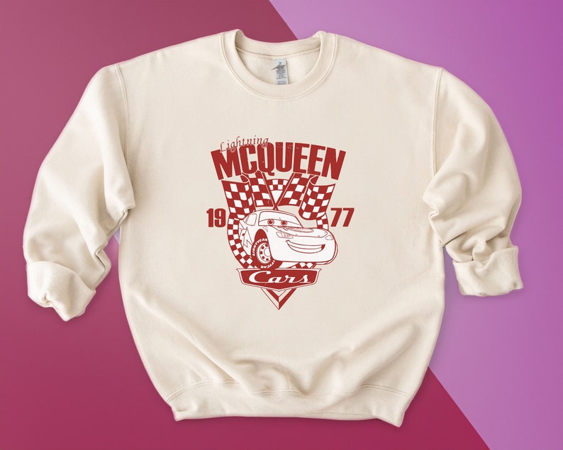 Puede incluir: Una sudadera de color crema con un gr&aacute;fico rojo de Rayo McQueen de la pel&iacute;cula Cars de Disney Pixar. El gr&aacute;fico incluye el texto "Lightning McQueen", "19", "77" y "Cars".