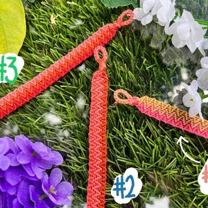 Könnte beinhalten: Drei Freundschaftsarmbänder in Rosatönen, Orange und Gelb. Die Armbänder sind mit einem Chevron-Muster gefertigt und mit #1, #2 und #3 gekennzeichnet.