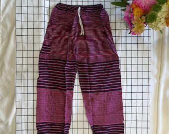 May include: Purple and black striped pants with a drawstring waist. The pants have a relaxed fit and are made of a lightweight fabric. The stripes are horizontal and evenly spaced. The pants are laid flat on a white grid.