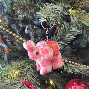 May include: A pink and white checkered elephant keychain with a silver key ring. The elephant is hanging on a Christmas tree.