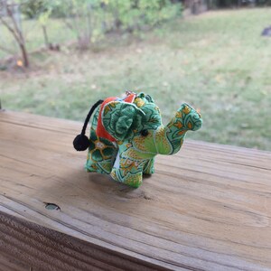 May include: A small green, orange, and yellow fabric elephant with a black tail. The elephant is a keychain or ornament.