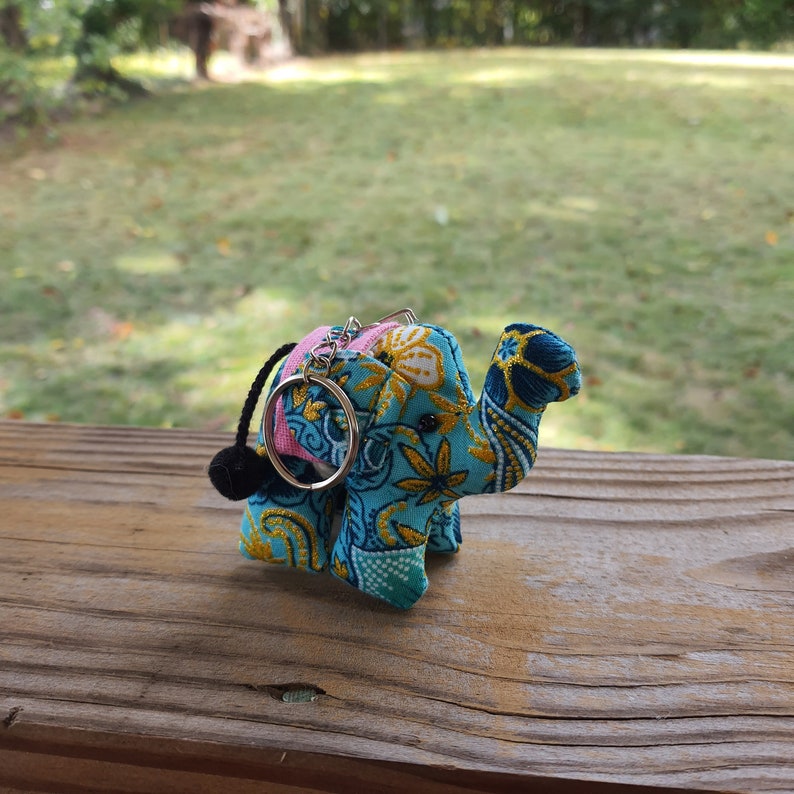 May include: A blue, yellow, and pink patterned elephant keychain with a black tassel. The elephant is made of fabric and has a silver key ring.