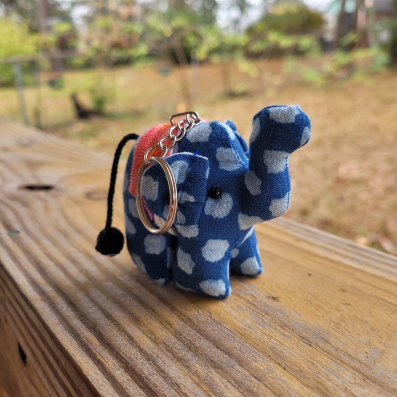 May include: A blue and white polka dot elephant keychain with a silver key ring and a red and orange strap.