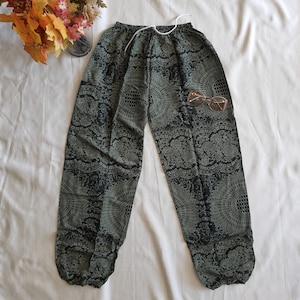 May include: Black and green patterned pants with a drawstring waist and elastic cuffs. The pants have a floral and geometric design.