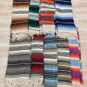 May include: A collection of ten rectangular woven blankets featuring various color combinations including brown, green, orange, blue, gray, red, and white. Each blanket displays horizontal stripes and a geometric pattern with fringe at the ends.