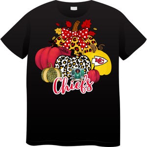 Op de afbeelding: Zwart T-shirt met een herfstontwerp met pompoenen en een strik. De pompoenen hebben verschillende patronen, waaronder luipaardprint en het logo van de Kansas City Chiefs. Het woord "Chiefs" is in rode letters geschreven.